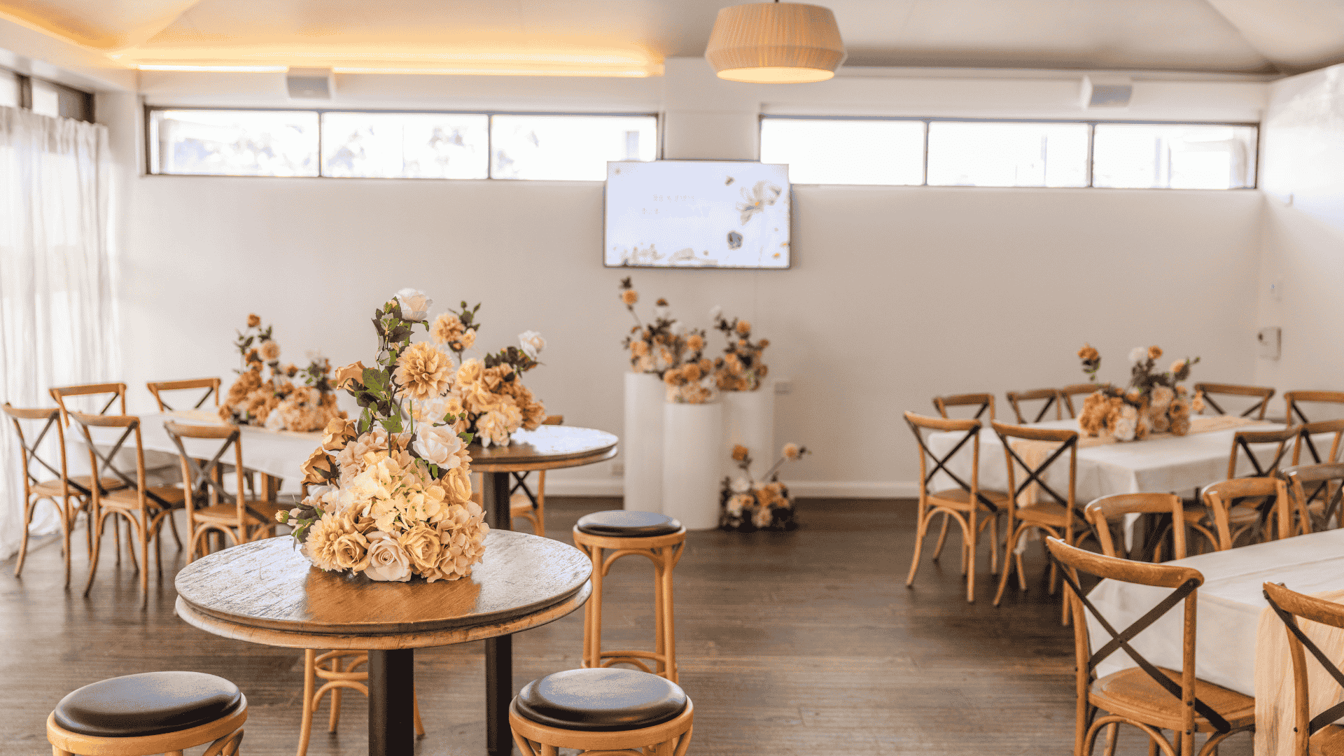 room with high ceilings, round and long tables, white curtains, and floral table arrangements