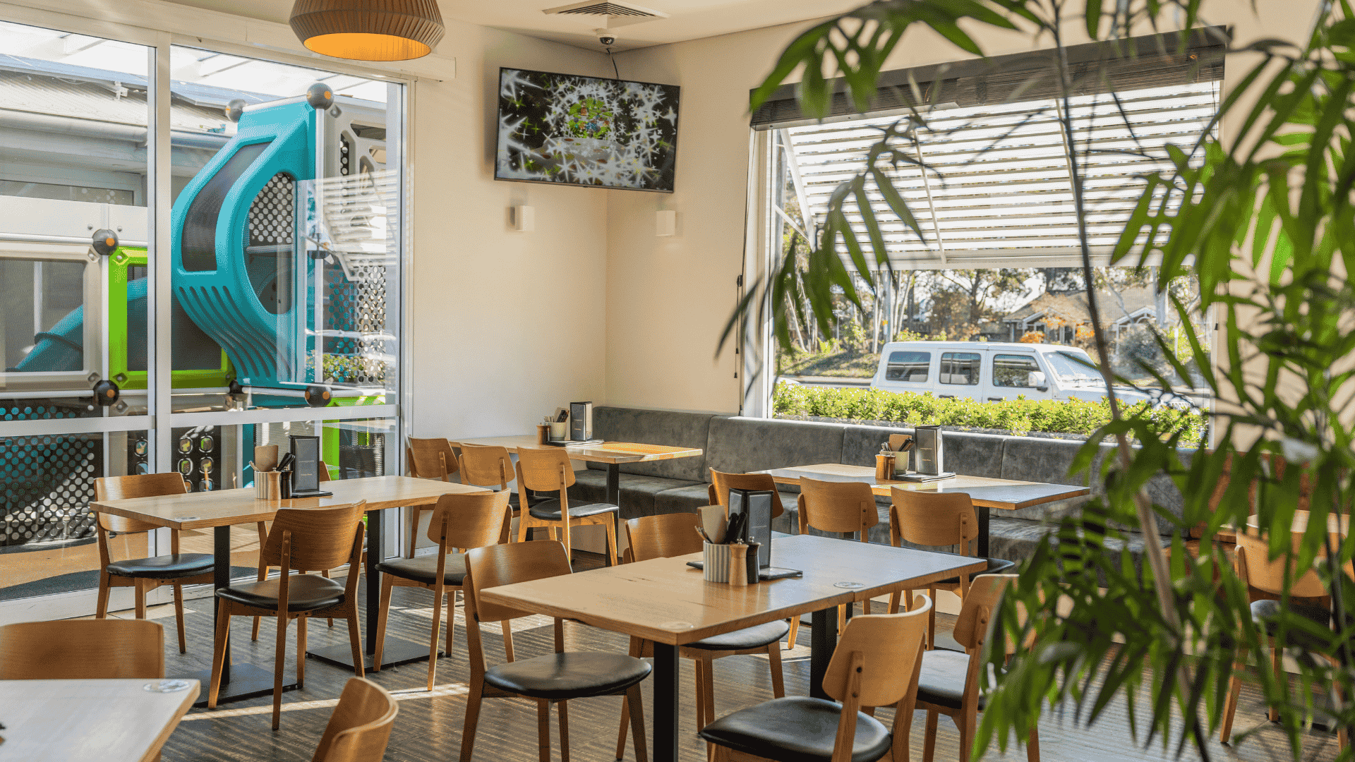 dining area with wooden tables and chairs, next to an enclosed kids play area behind large windows